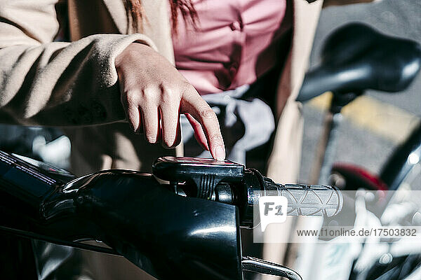 Businesswoman unlocking electric bicycle at parking station