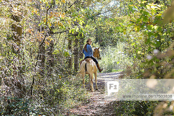 Young woman looking over shoulder while horseback riding in forest on sunny day