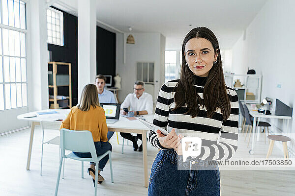 Businesswoman holding tablet PC with colleagues working in office