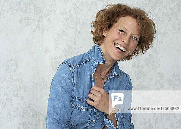 Happy woman wearing denim shirt in front of wall at home