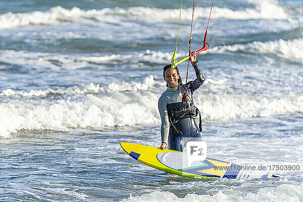 Glückliche Frau mit Kiteboard  die den Griff eines Drachenfallschirms im Wasser hält