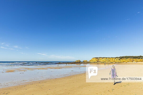 Female tourist walking along sandy coastal beach in summer