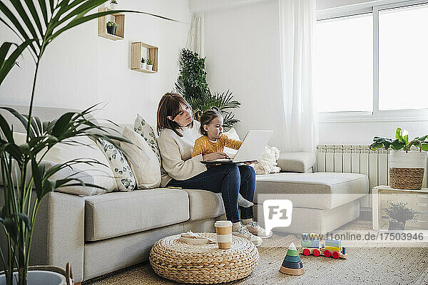Mother sitting with daughter and using laptop in living room