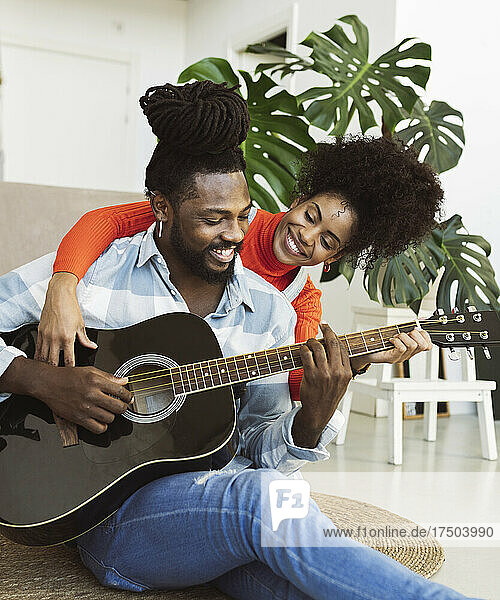Lächelnde junge Frau lernt Gitarre von ihrem Freund