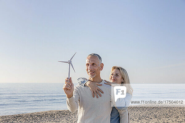 Woman embracing man holding wind turbine model at beach