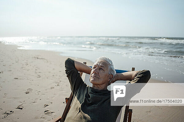 Senior man looking up relaxing on chair at beach