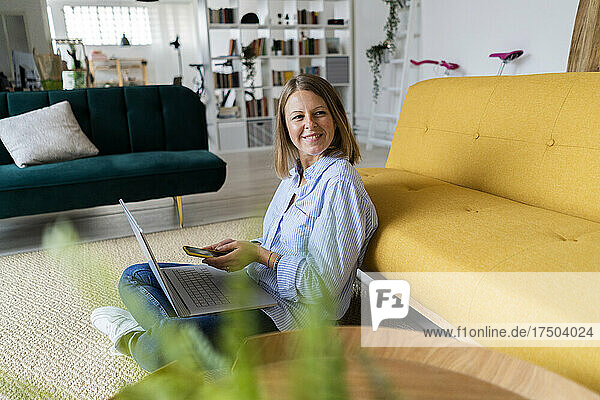 Woman with mobile phone and laptop working at home