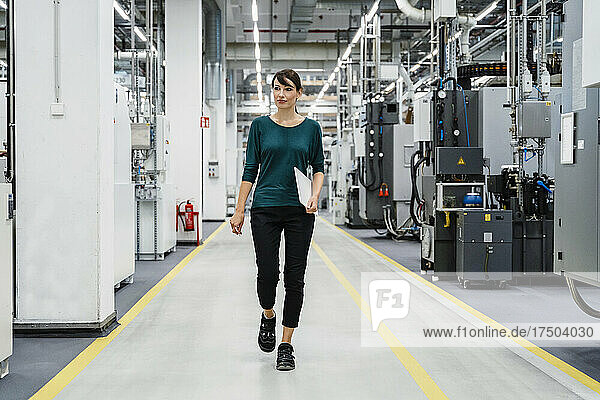 Businesswoman with tablet PC walking amidst industrial equipment