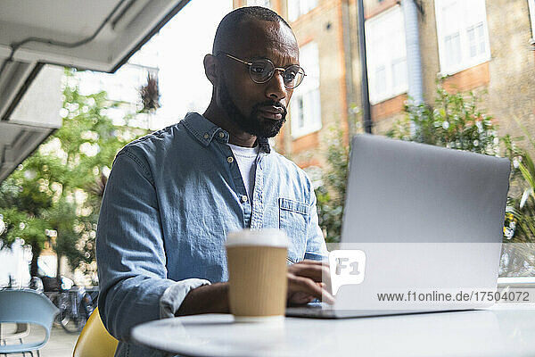 Man using laptop at table in sidewalk cafe