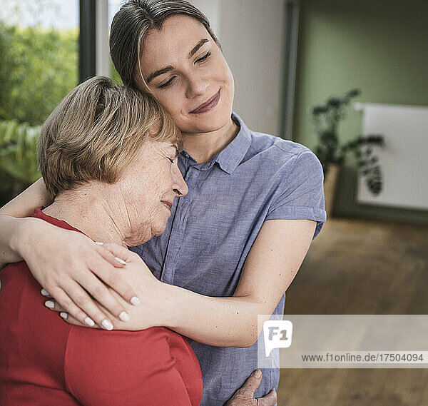 Senior woman hugging young caregiver at home