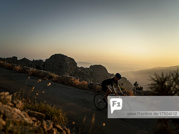 Athlete cycling on mountain road at sunset