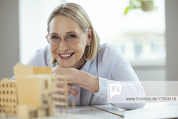 Smiling businesswoman with hand on chin at desk