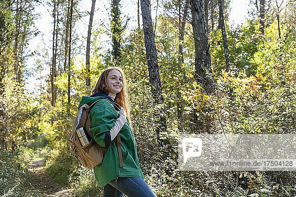 Smiling woman with backpack looking away while hiking in forest