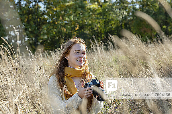 Lächelnde Frau mit Kamera  die an einem sonnigen Tag wegschaut