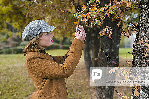 Young woman wearing beret examining autumn leaves in park