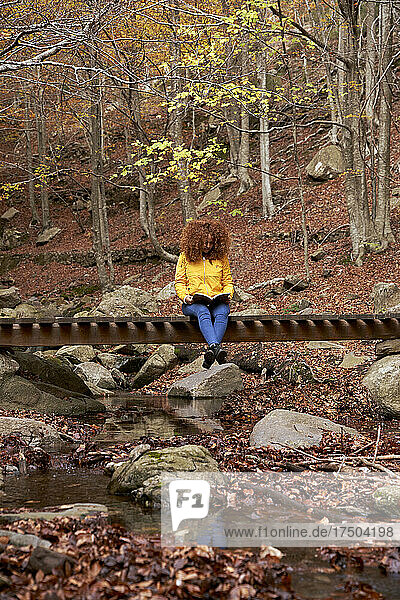 Young woman reading book on wooden bridge in forest