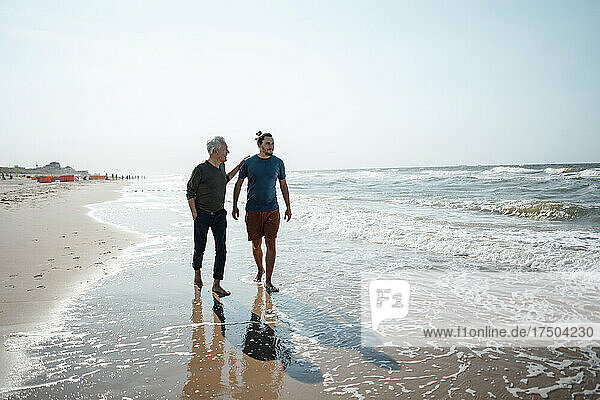 Father and son walking together on wet sand at beach