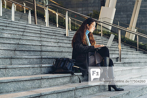 Berufstätige Frau benutzt Laptop und sitzt auf Stufen