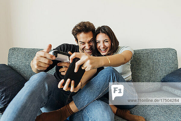 Cheerful girlfriend and boyfriend playing video game with controller at home