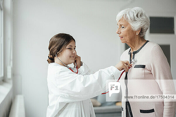 Granddaughter with stethoscope checking grandmother at home