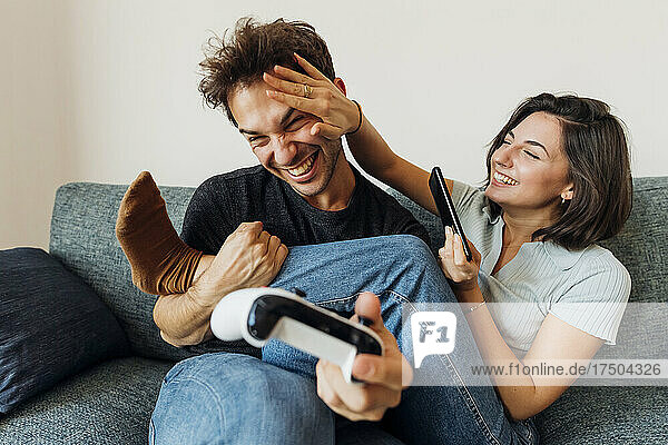 Playful young couple with game controller and smart phone at home