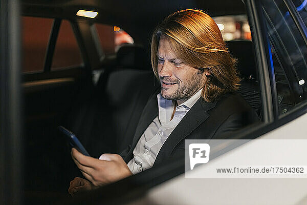 Businessman using smart phone in car at night