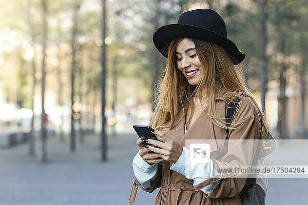 Smiling woman wearing trenchcoat using mobile phone in city