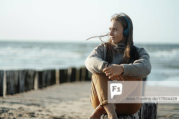 Woman listening music on headphones sitting at beach