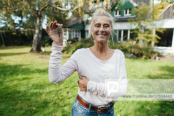 Happy woman holding house key at backyard