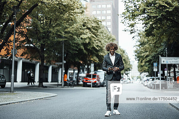Businessman using mobile phone walking on city street