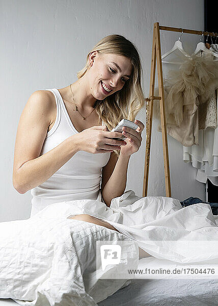 Lächelnde Frau  die SMS über ihr Smartphone im Bett sendet