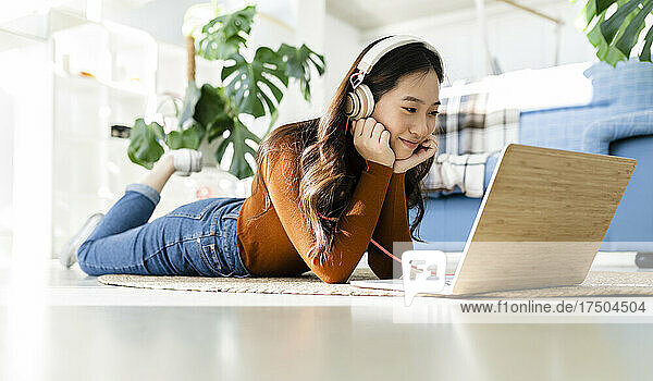 Smiling freelancer with headphones watching laptop on floor