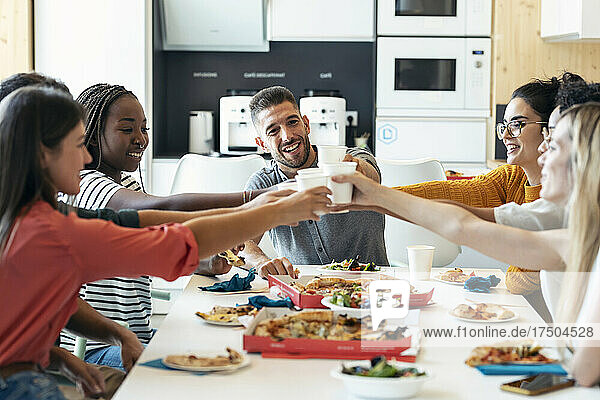 Smiling multiracial colleagues toasting drinks at cafeteria in lunch break