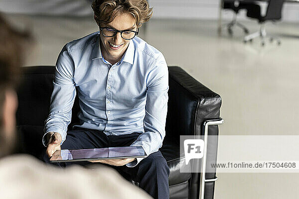 Smiling young businessman with digital tablet working on business strategy in lobby