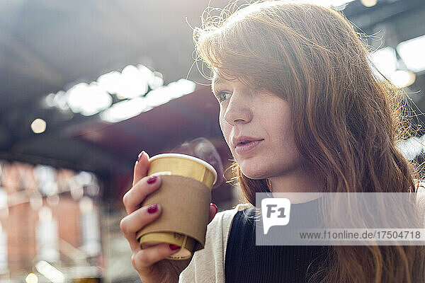 Young woman having coffee in disposable cup at cafe