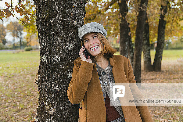Happy woman talking on mobile phone at tree in park