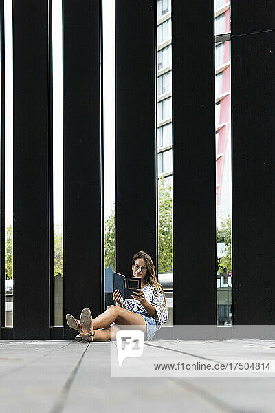 Young woman reading book outside modern building