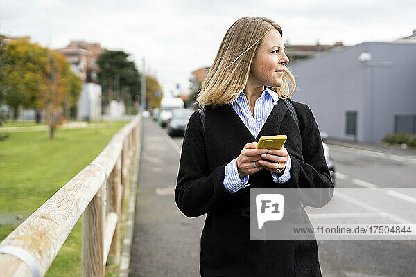 Blond woman holding smart phone on road