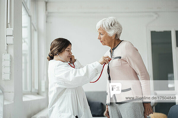 Girl listening to woman heartbeat with stethoscope at home