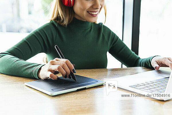 Smiling freelancer using digitized pen on graphics tablet at table in cafe