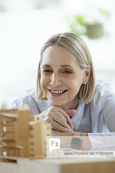 Female architect with hand on chin looking at model in office