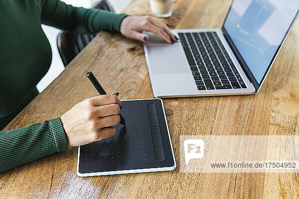 Freelancer with laptop using graphics tablet at coffee shop