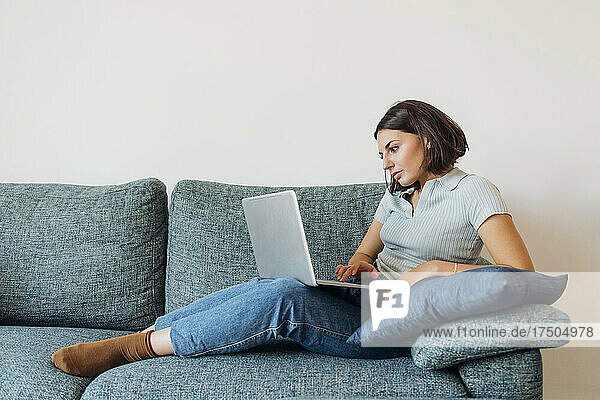 Young female freelancer working on laptop in living room at home