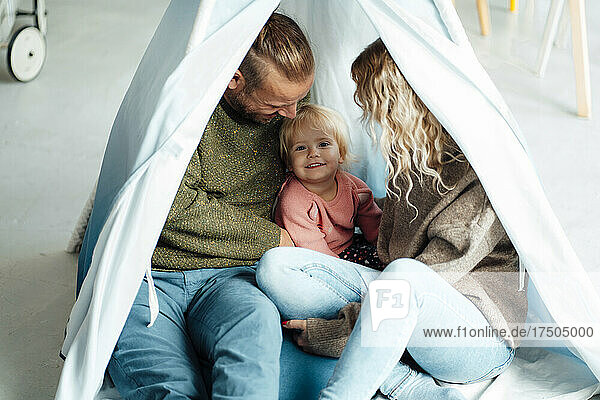 Playful daughter sitting with parents inside tent at home