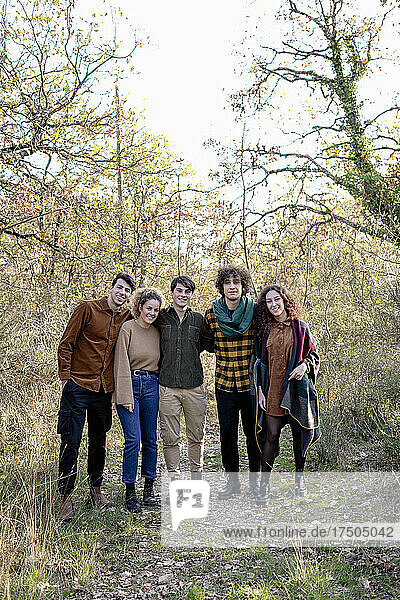 Smiling friends standing together in autumn forest on weekend