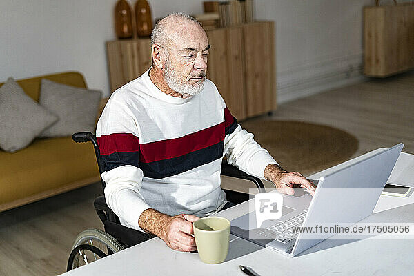 Disabled businessman with coffee cup using laptop at home office