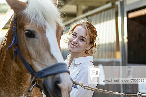 Lächelnde Frau blickt auf Pferd im Stall