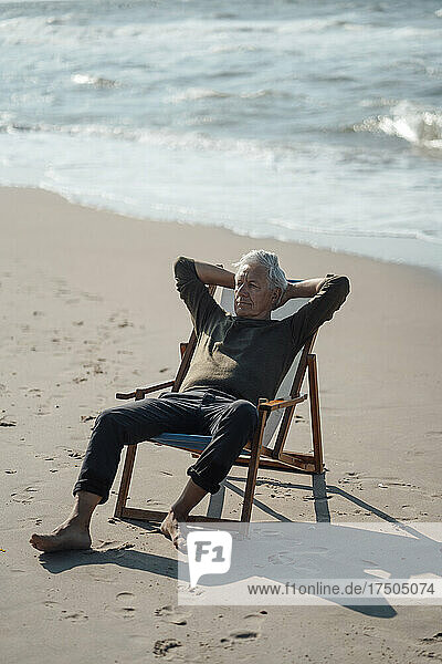 Senior man with hands behind head on chair at beach