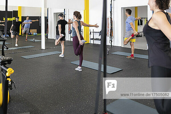 Sportler strecken sich auf einem Bein und trainieren vor dem Spiegel im Fitnessstudio