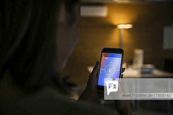 Woman using smart phone with light bulb icon screen at home